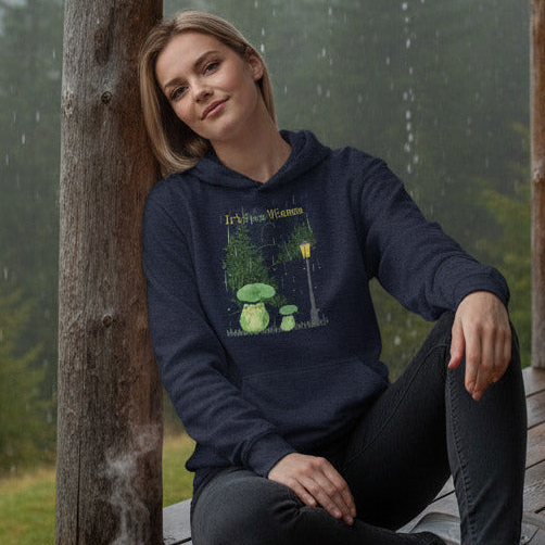 Woman wearing a hoodie with a forest design, sitting against a tree in a natural setting.