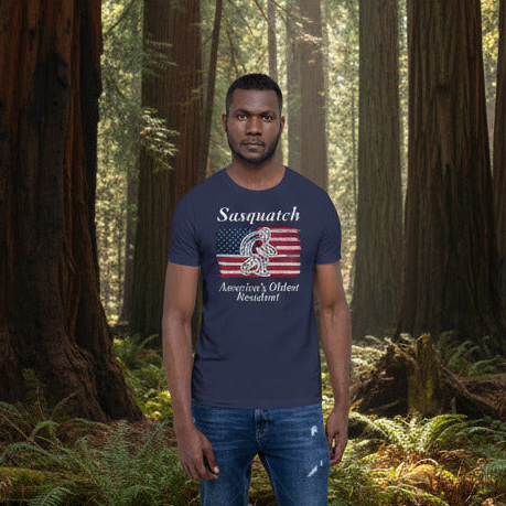 Man wearing a blue t-shirt with a Sasquatch design in a forest setting