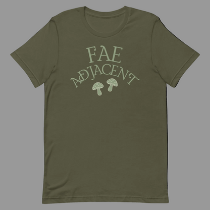 An olive green short-sleeve t-shirt with a light sage green graphic on the chest that reads 'FAE ADJACENT' above two small mushrooms, shown on a plain white background.