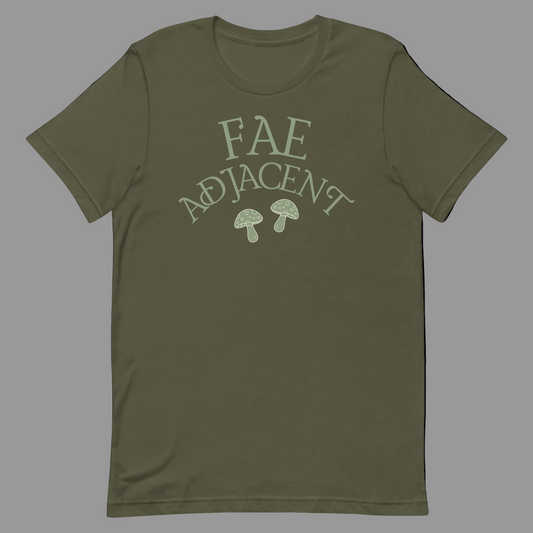 An olive green short-sleeve t-shirt with a light sage green graphic on the chest that reads 'FAE ADJACENT' above two small mushrooms, shown on a plain white background.