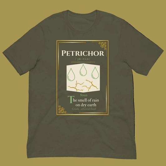 An olive green crewneck t-shirt featuring a graphic print styled like a vintage dictionary entry for 'Petrichor'. The graphic includes a gold border, three green rain drops, and the definition 'The smell of rain on dry earth' with 'Greek word root: petrichor'.