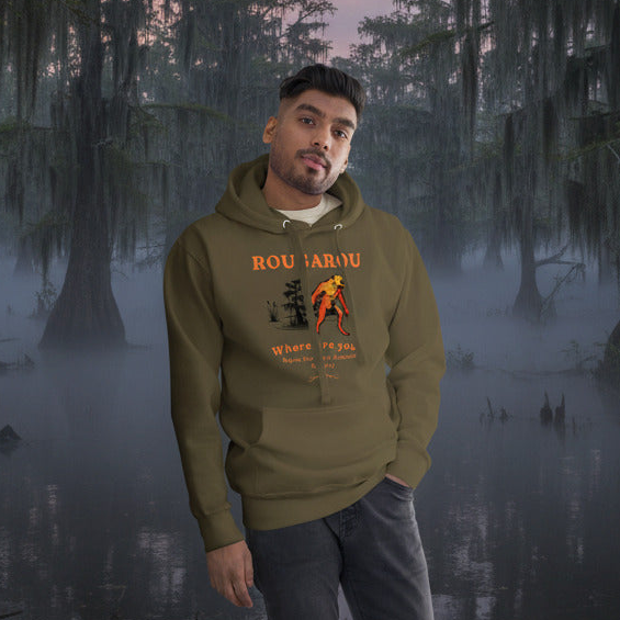 Man wearing a green hoodie with a rougarou graphic design standing in a misty swamp.