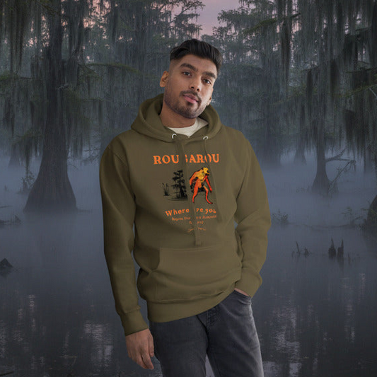 Man wearing a green hoodie with a rougarou graphic design standing in a misty swamp.